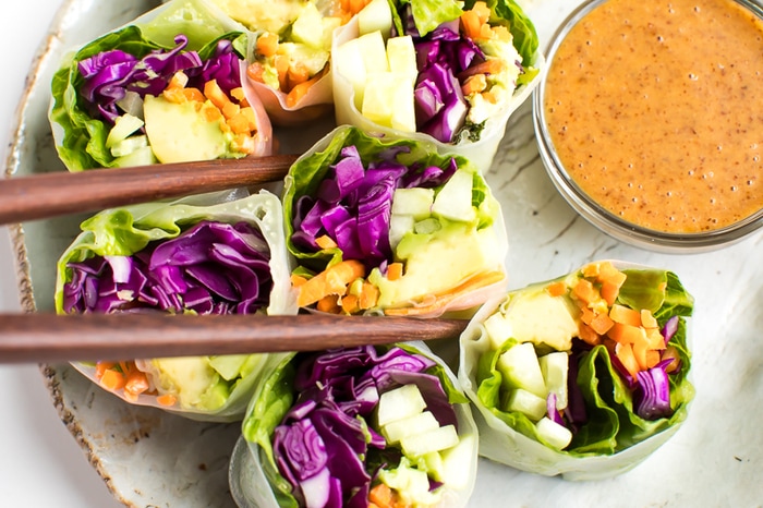 PIN THIS --> EASY Vegetable Spring Rolls with a Delicious Peanut Sauce Fresh vegetables spring rolls with homemade peanut sauce being picked up with wooden chopsticks.