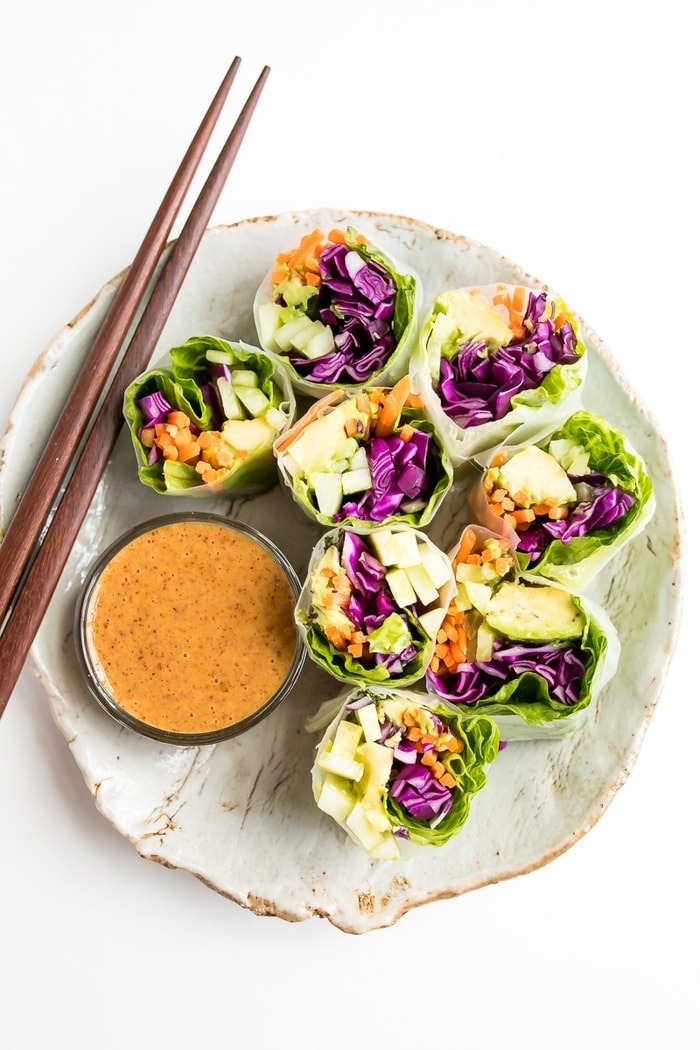 PIN THIS --> EASY Vegetable Spring Rolls with a Delicious Peanut Sauce Fresh vegetables spring rolls on a rustic plate with homemade peanut sauce and wooden chop sticks.