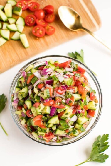 A serving of salad in a glass bowl with cherry tomatoes, diced cucumber, and red onion.