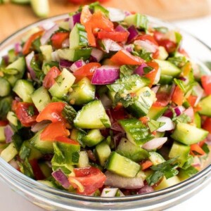 A large glass bowl filled with Israeli salad, a blend of tomatoes, cucumbers and red onion.