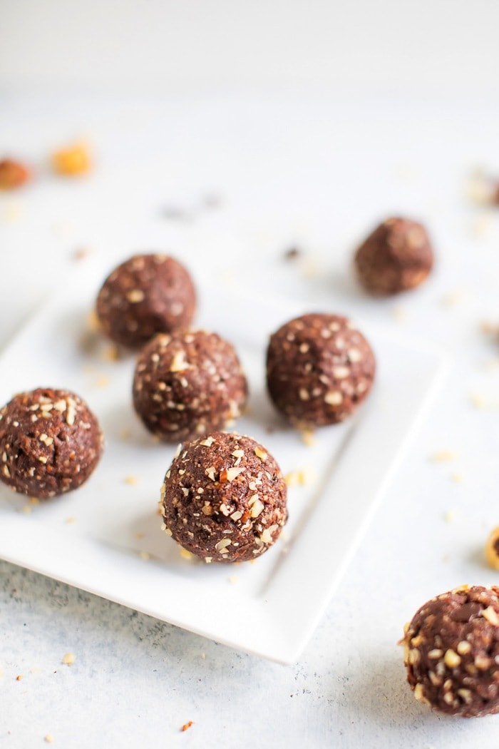 PIN THIS --> Healthy Homemade Ferrero Rocher Bites Homemade chocolate hazelnut energy bite in front with additional energy bites in the background on a white plate.