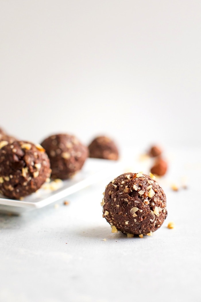 PIN THIS --> Healthy Homemade Ferrero Rocher Bites Homemade chocolate hazelnut energy bite in front with additional energy bites in the background on a white plate.