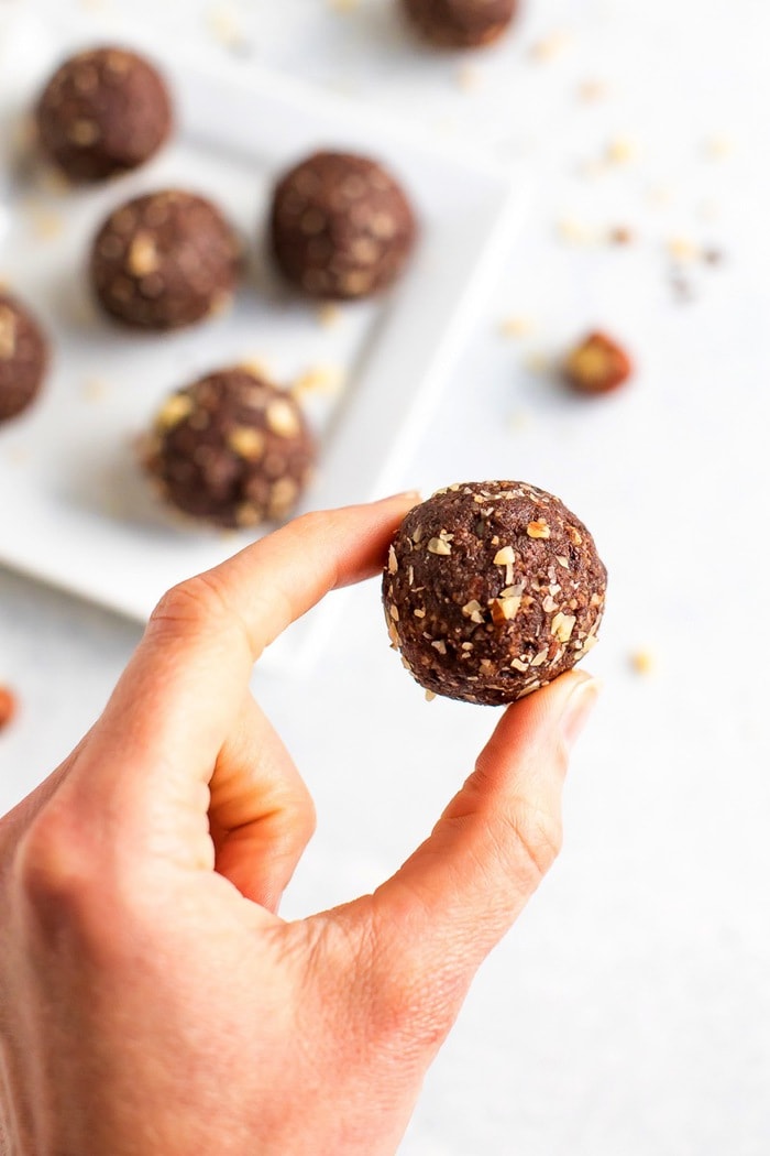 PIN THIS --> Healthy Homemade Ferrero Rocher Bites Homemade chocolate hazelnut energy bite being held by a woman's hand.