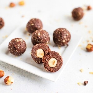 Homemade chocolate hazelnut energy bite in front, chopped in half to show the hazelnut in the center of the bite.