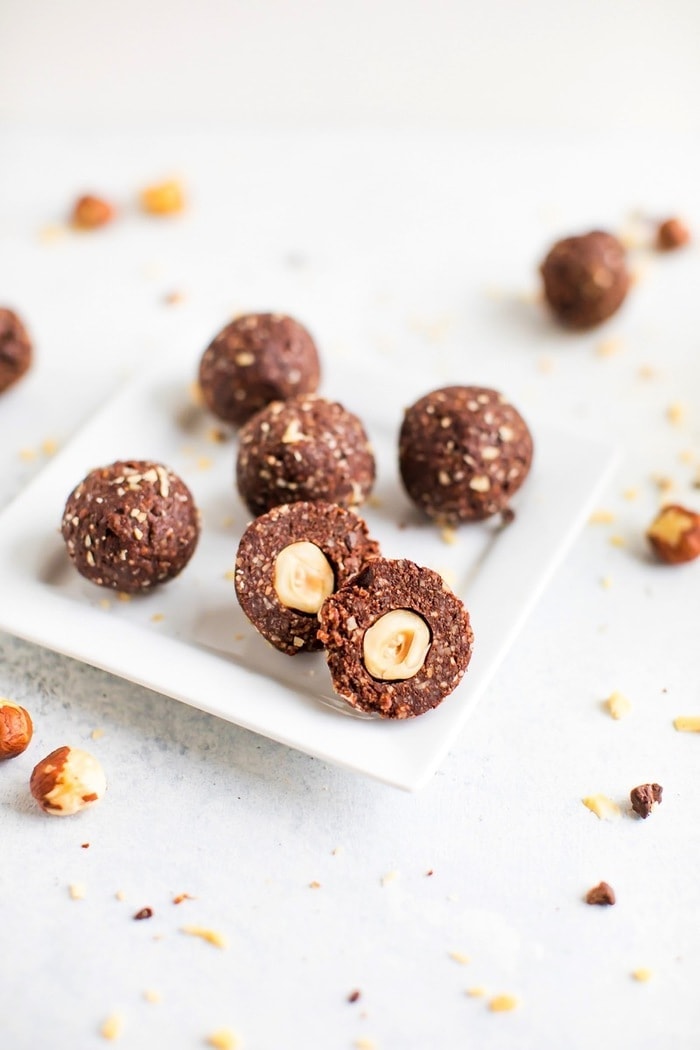 PIN THIS --> Healthy Homemade Chocolate Hazelnut Energy Bites Homemade chocolate hazelnut energy bite in front, chopped in half to show the hazelnut in the center of the bite.