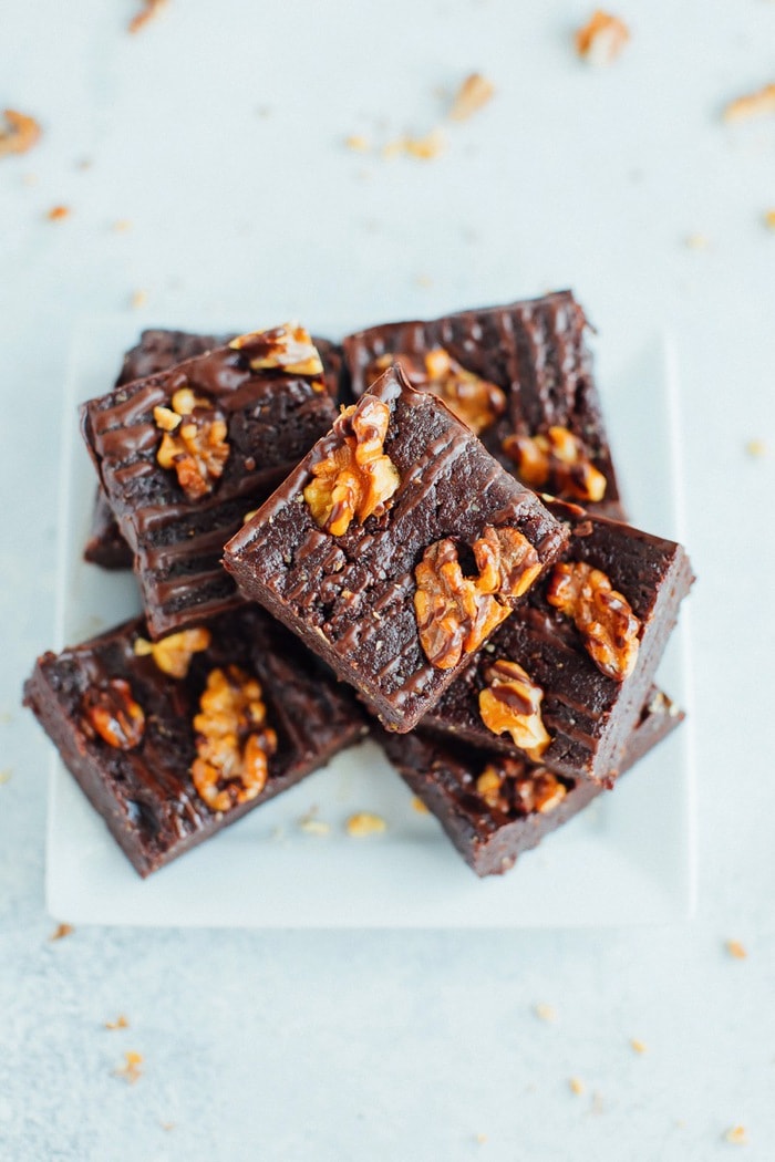 PIN THIS --> 5-Ingredient No Bake Brownies No bake brownies topped with walnuts and a chocolate drizzle on a small white square plate.
