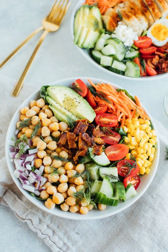 Vegan cobb salad in a white bowl with two gold forks in the background.