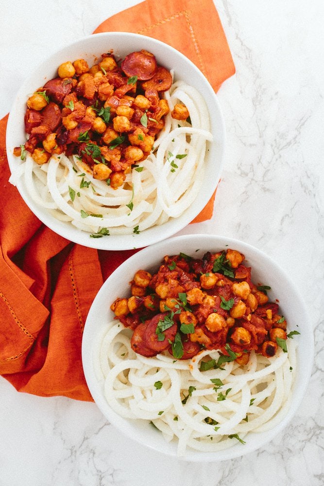 PIN THIS--> 12 Healthy Jicama Recipes Chickpeas and chorizo in a bowl on top of jicama spiralized noodles. Two bowls of food are on top of a cloth napkin.