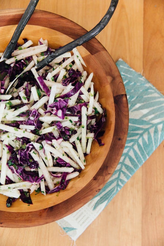 PIN THIS--> 12 Healthy Jicama Recipes Wooden bowl filled with jicama and purple cabbage slaw with two metal serving spoons.