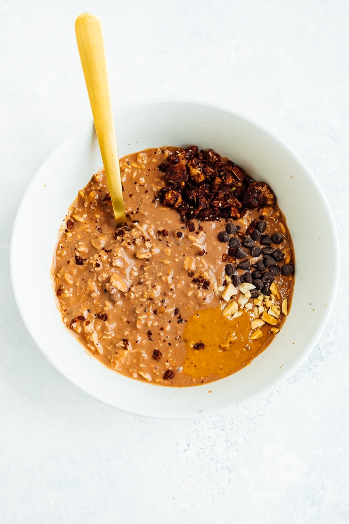 PIN THIS --> Peanut Butter Cup Overnight Oats A white bowl filled with chocolate peanut butter overnight oats topped with peanut butter, chocolate chips and granola.