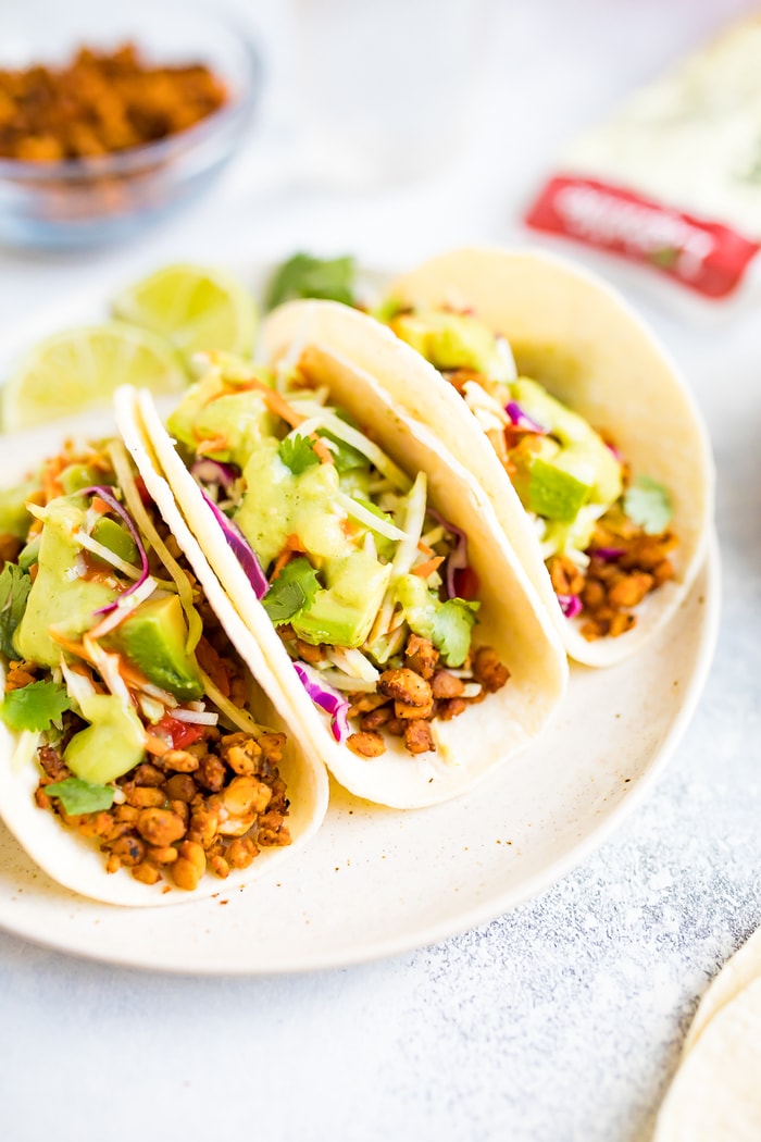 PIN THIS --> Tempeh Tacos Three tempeh tacos on a white plate, topped with avocado and cilantro.