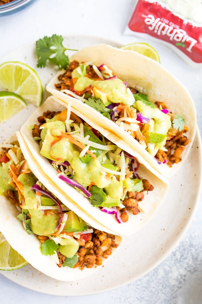 PIN THIS --> Tempeh Tacos Three tempeh tacos with cilantro, avocado and tomatillo dressing on a white plate.