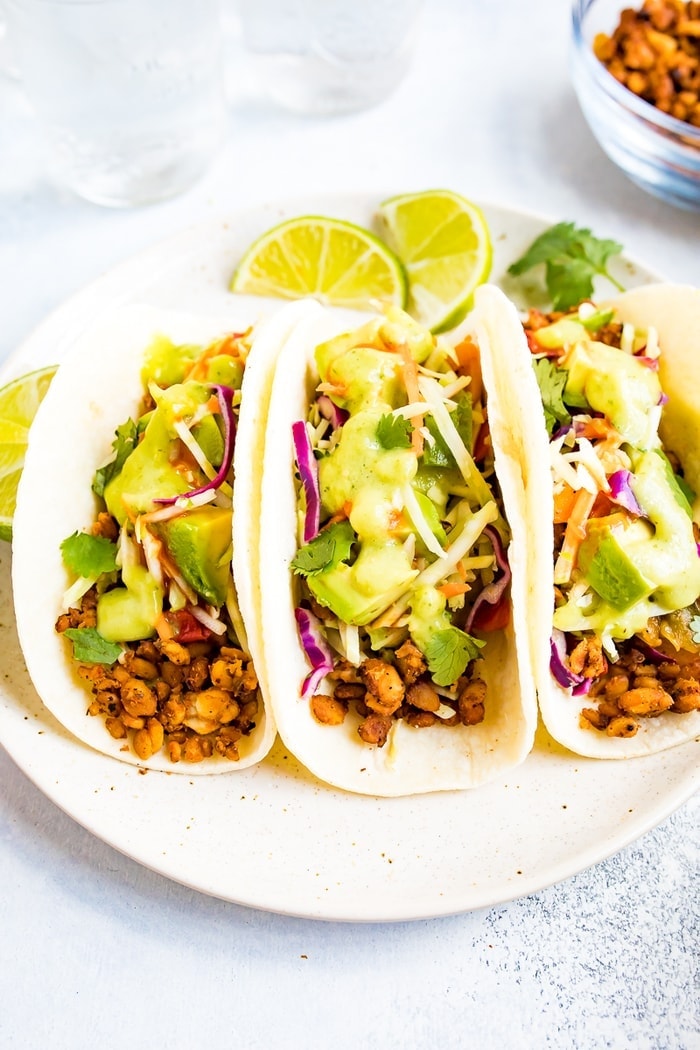 PIN THIS --> Tempeh Tacos Three tempeh tacos with avocado and tomatillo dressing on a plate.