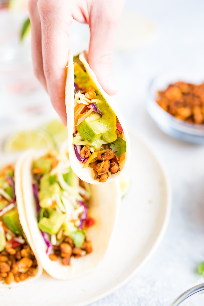 PIN THIS --> Tempeh Tacos Hand holding one tempeh taco topped with avocado, cilantro, and tomatillo dressing.