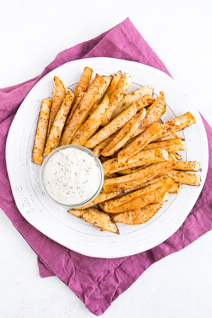 PIN THIS--> Baked Turnip Fries A white plate of turnip fries and a jar of ranch dip on top of a purple napkin.