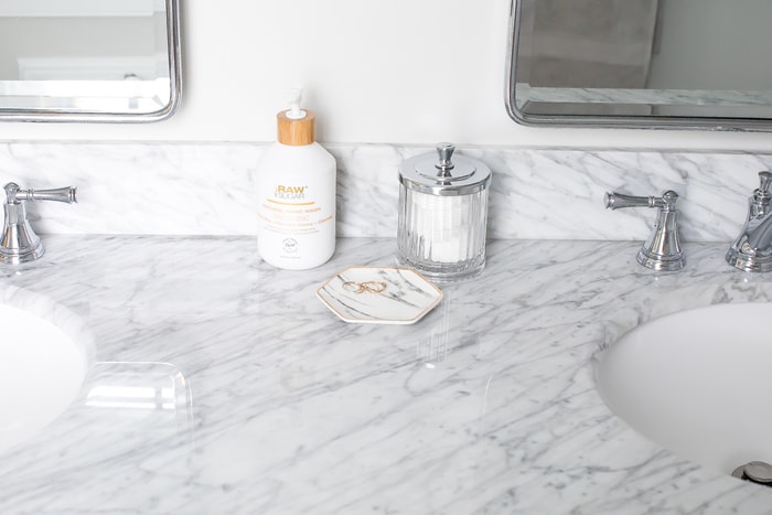 A marble countertop with a glass container for cotton swabs and a lotion bottle.