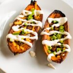 A serving of sweet potato skins filled with vegan cheese, vegan bacon, sour cream and chives on a white plate.