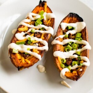 A serving of sweet potato skins filled with vegan cheese, vegan bacon, sour cream and chives on a white plate.