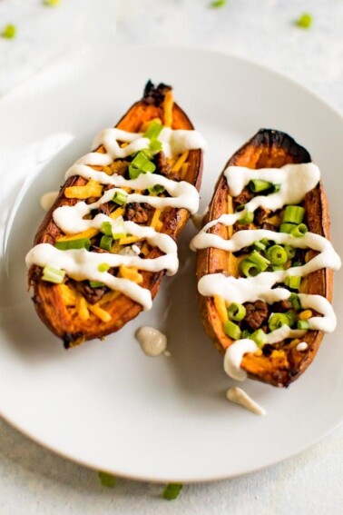 A serving of sweet potato skins filled with vegan cheese, vegan bacon, sour cream and chives on a white plate.