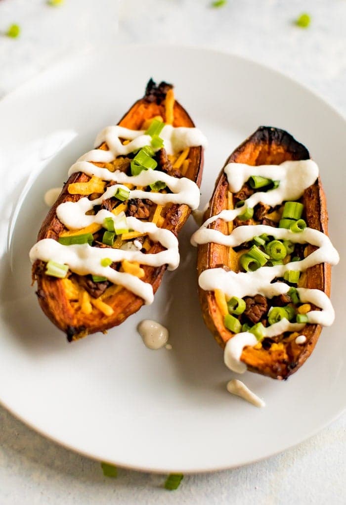A serving of sweet potato skins filled with vegan cheese, vegan bacon, sour cream and chives on a white plate.