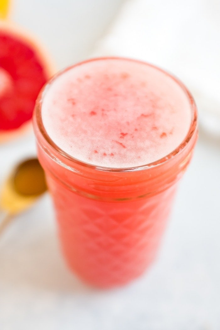 A glass jar with a grapefruit drink filled to the top.