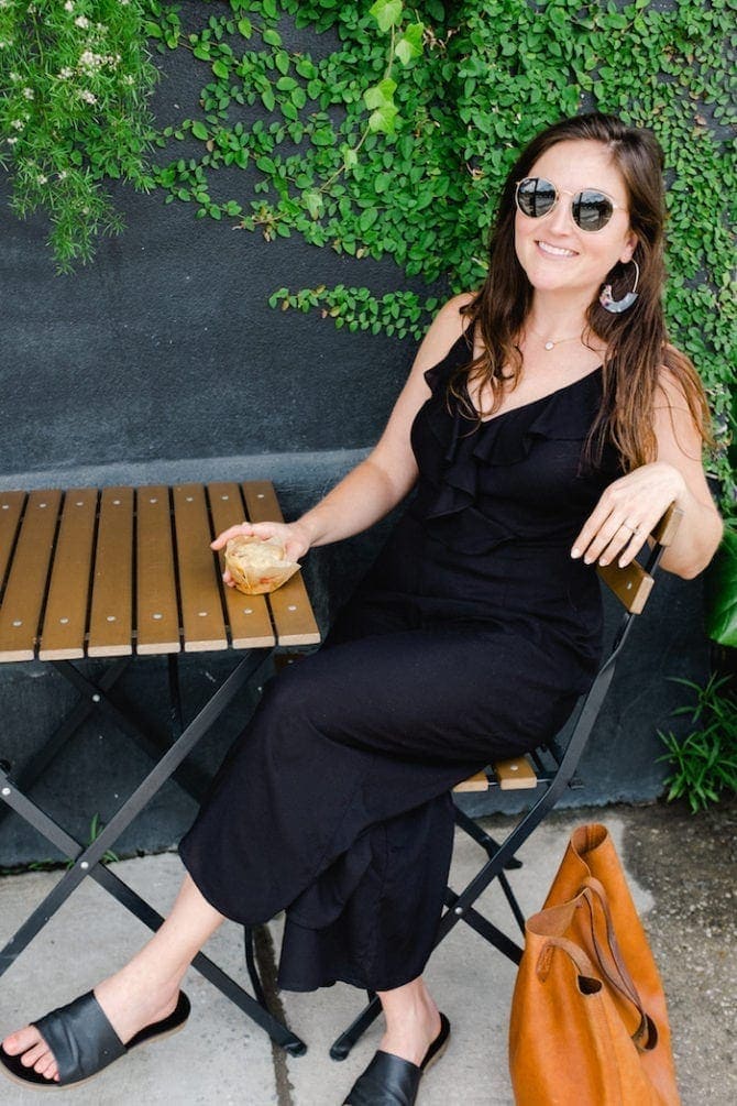 Woman sitting on a cafe patio with muffin in her hand.