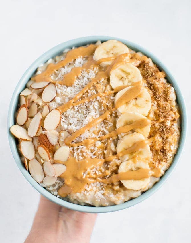 Bowl of cottage cheese protein oatmeal topped with sliced almonds, coconut flakes, banana, flax seeds and peanut butter.