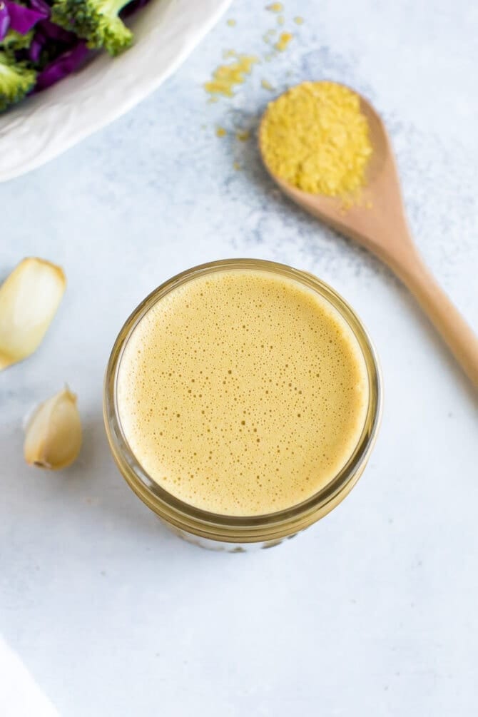 Nutritional yeast dressing in a small mason jar. To the right is a small wooden spoon with a scoop of nutritional yeast.