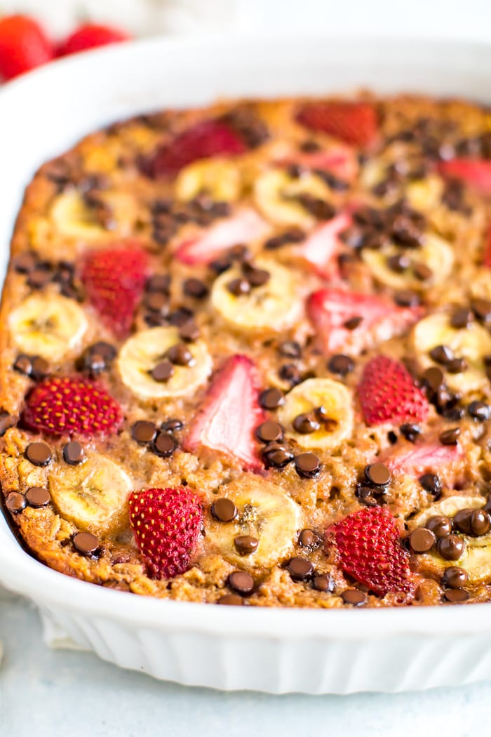 Close up photo of baked oatmeal with fresh strawberries, banana and chocolate chips in a square baking dish.