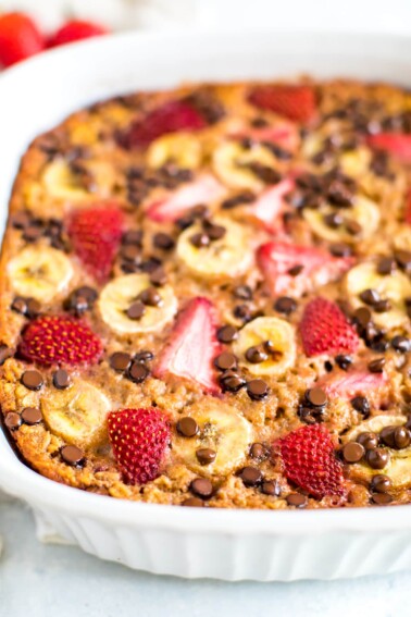 Baked oatmeal with fresh strawberries, banana slices and chocolate chips in a baking dish.