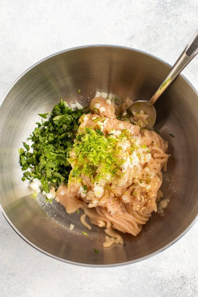 Mixture of ingredients for cilantro lime chicken burgers: ground chicken, lime zest, and cilantro.