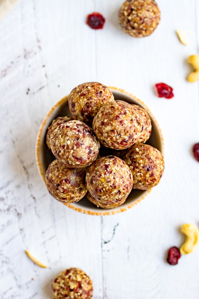 Bird's eye view of a bowl full of cranberry energy bites. On the table are some nuts and dries cranberries.