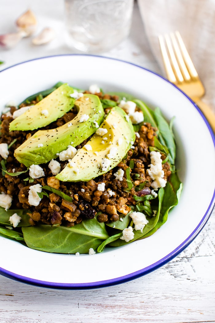A plate with a bed of fresh spinach topped with a warm Mediterranean salad, topped with feta and avocado.