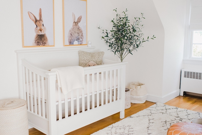 Baby girl neutral nursery with bunny prints above crib.