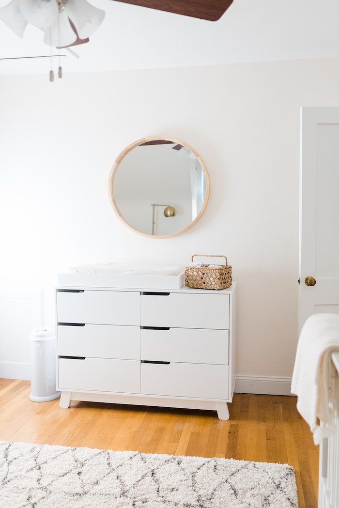Baby girl nursery with a white dresser changing station and round mirror above.