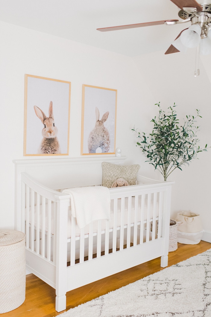 Baby girl neutral nursery with bunny prints above crib.