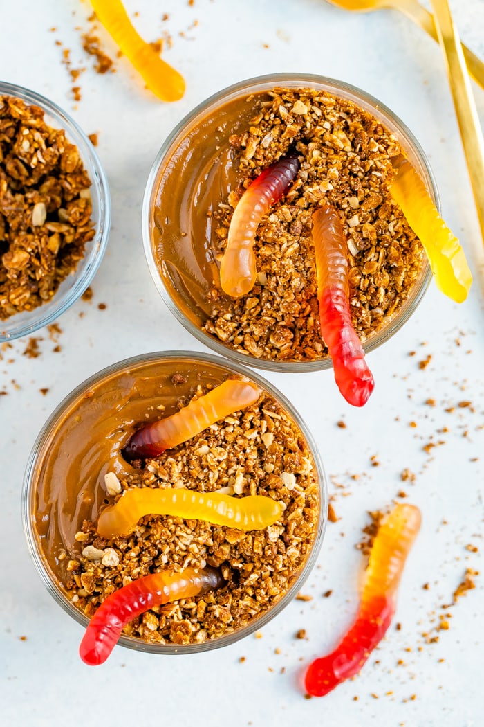 Two glass cups with chocolate dirt pudding topped with granola and gummy worms.
