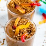 Two glass cups served with chocolate dirt pudding topped with granola and gummy worms.