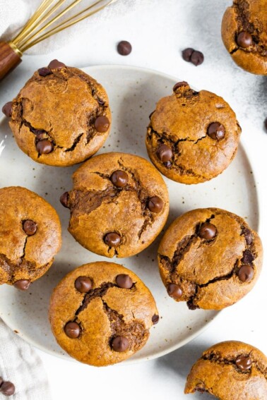 Six flourless pumpkin muffins with chocolate chips served on a large plate.