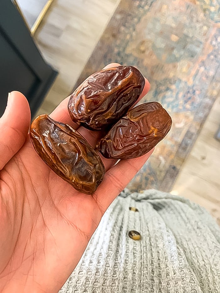 Three medjool dates in a palm of a women's hand.