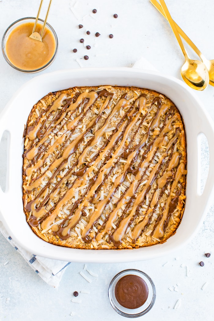 Square dish with baked oatmeal topped with caramel and chocolate drizzles and coconut flakes.