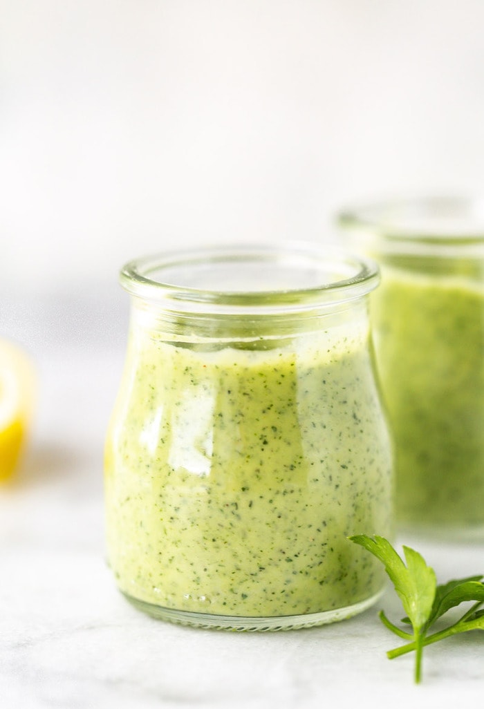 Straight on photo of two glass jars with avocado ranch dressing on a marble board.