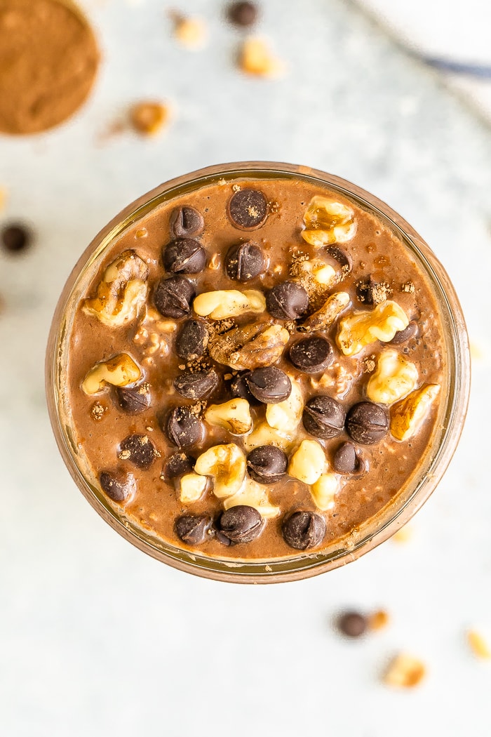 Overhead photo of chocolate brownie batter overnight oats in a mason jar. Topped with walnuts and chocolate chips.