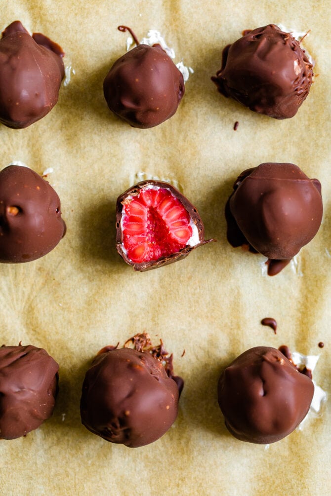 Chocolate and yogurt covered frozen raspberries on parchment paper.