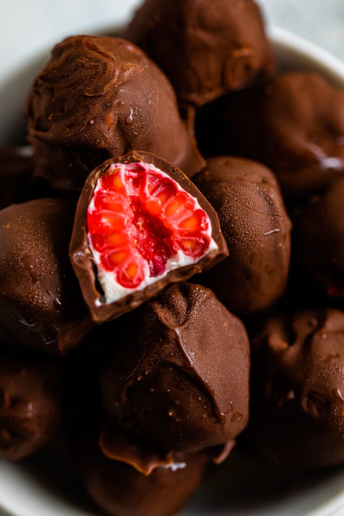 Bowl of chocolate covered frozen raspberries with yogurt. One raspberry is cut in half.