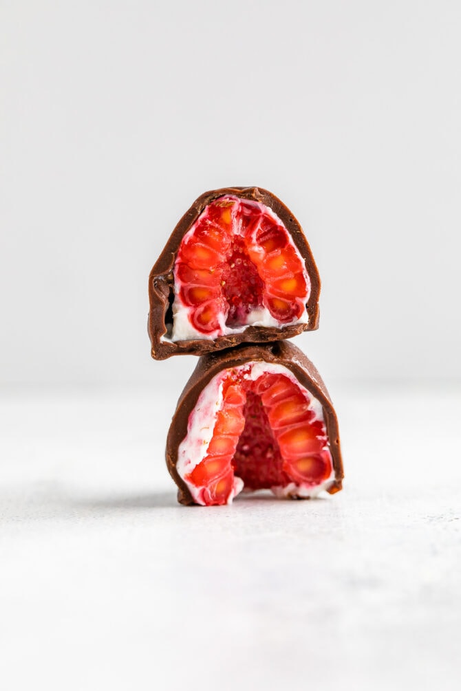 A chocolate covered and yogurt dipped frozen raspberry cut in half and stacked on top of each other.