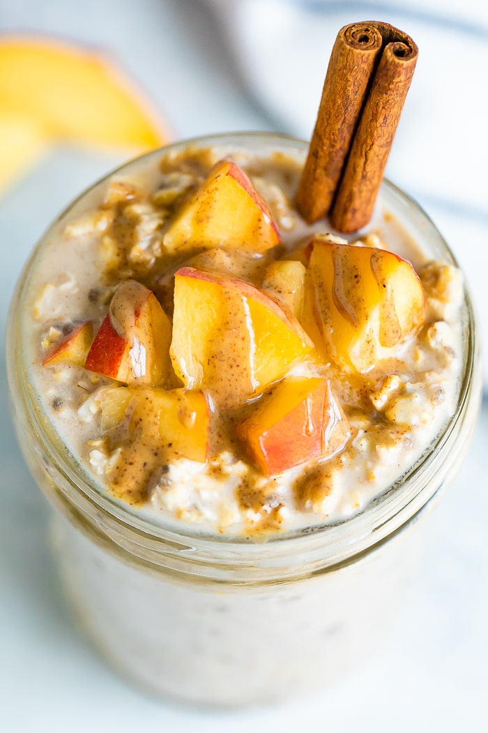 Overhead photo of peach overnight oats topped with peaches, almond butter and a cinnamon stick.