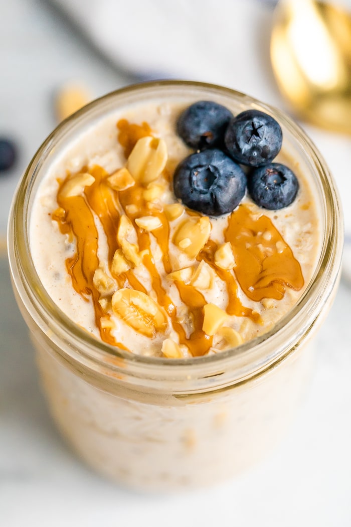 Overhead photo of peanut butter overnight oats in a mason jar topped with blueberries, chopped peanuts and a peanut butter drizzle.