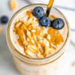 A serving of peanut butter overnight oats in a mason jar topped with fresh blueberries, chopped peanuts and a peanut butter.