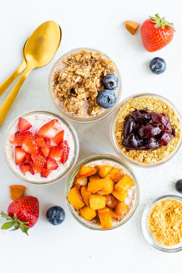 Overhead photo with four mason jars with different overnight oat flavors: cherry cheesecake, peach pie, strawberry and blueberry crumble
